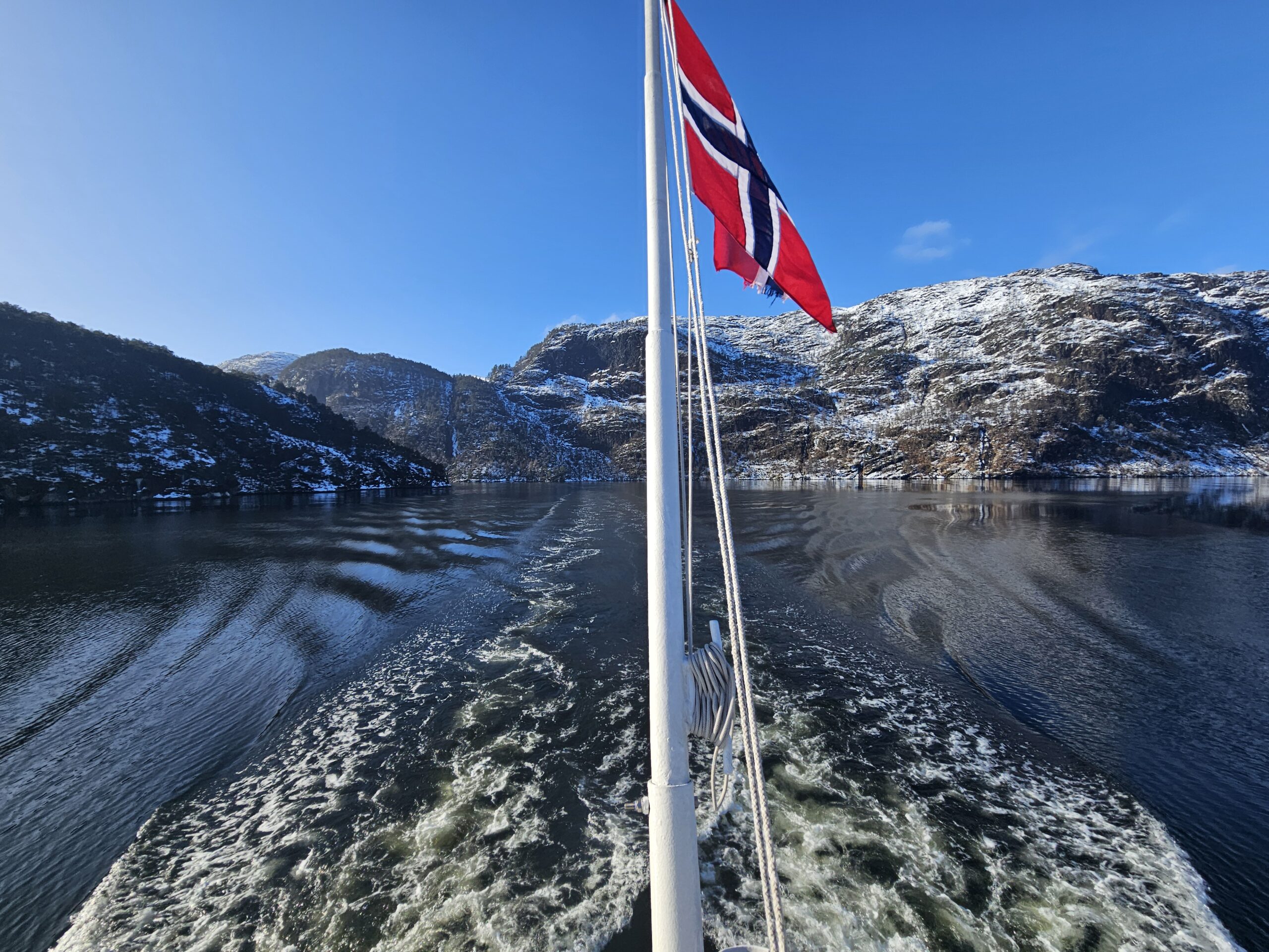 Back of the Mostraumen Fjord Cruise on a sunny day, with Norwegian flag and fjords in the background.